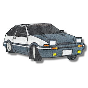 Può includere: Una toppa ricamata di un'auto sportiva giapponese classica, con uno schema di colori bianco e grigio. L'auto ha fari neri e frecce gialle.