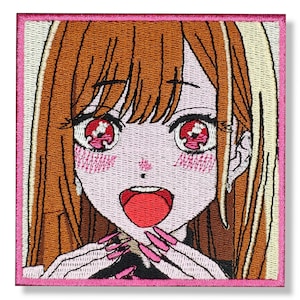 Peut inclure: Patch brodé représentant une fille de dessin animé anime avec de longs cheveux bruns, des joues roses et des yeux rouges. Elle sourit la bouche ouverte et ses mains sont devant son visage avec des ongles roses.