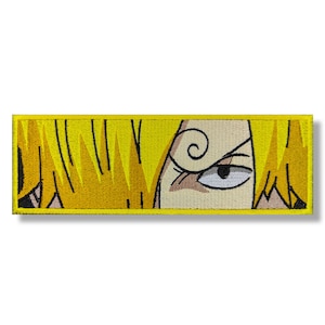 Può includere: Primo piano di una toppa ricamata gialla con un solo occhio con un disegno a spirale sopra. L'occhio guarda a destra.