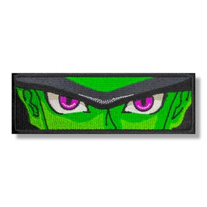 May include: Green and black embroidered patch with a close-up of a character's eyes. The eyes are white with pink pupils.