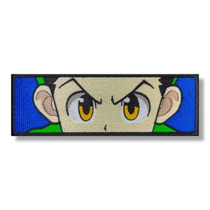 Puede incluir: Parche bordado con un primer plano de la cara de un personaje de dibujos animados con cabello verde, ojos amarillos y una expresión seria. El fondo es azul y verde.