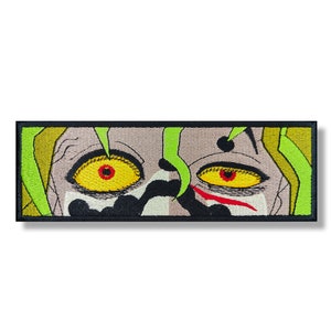 Puede incluir: Parche bordado con un primer plano de una cara con ojos amarillos y un fondo verde y negro.