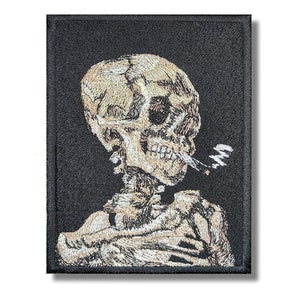 Może przedstawiać: Naszywka haftowana przedstawiająca szkielet palący papierosa. Naszywka jest na czarnym tle, a szkielet jest w kolorze beżowym.