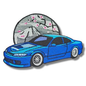 May include: Blue embroidered patch of a car with a cherry blossom tree and mountain in the background.