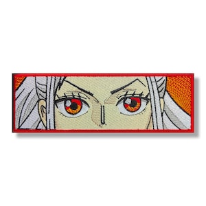 May include: Embroidered patch featuring a close-up of a woman's face with white hair and red eyes. The background is a gradient of orange and yellow.