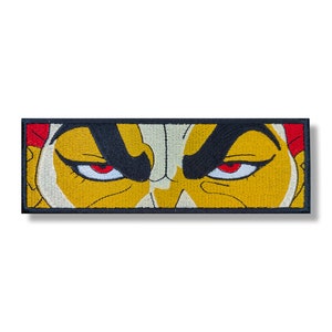 Peut inclure: Patch brodé représentant un gros plan sur le visage d'un personnage avec des yeux rouges et un fond jaune et noir.