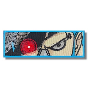 Puede incluir: Parche bordado con un primer plano de un ojo de personaje con un iris rojo incandescente. El personaje tiene un fondo oscuro texturizado y una tez marrón clara.