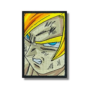 May include: Embroidered patch featuring a close-up of a determined character with spiky yellow hair and intense blue eyes. The patch has a black border and a beige background with detailed stitching.