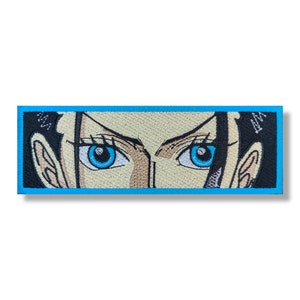 May include: Embroidered patch featuring a close-up of a woman's face with blue eyes. The patch has a black background and a light blue border.