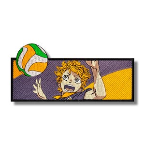 Op de afbeelding: Geborduurde patch met een volleybal en een personage met stekelig oranje haar, tegen een paarse en gele achtergrond. Het personage is in actie, met een open mond en een opgeheven arm, terwijl de volleybal erboven zweeft.