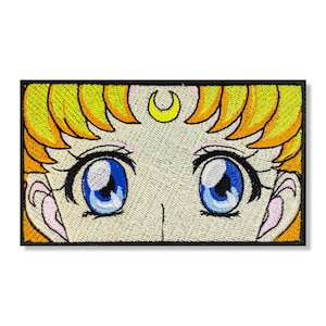 Può includere: Toppa ricamata con un primo piano degli occhi di un personaggio dei cartoni animati con una mezzaluna sopra. Il personaggio ha i capelli biondi e gli occhi azzurri.