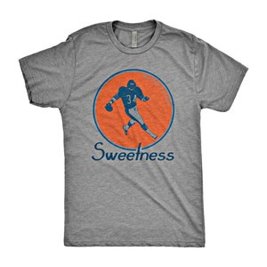 May include: A heather grey t-shirt with a vintage-style graphic of a football player in a blue uniform running with the ball. The graphic is surrounded by an orange circle with the text "Sweetness" below it.