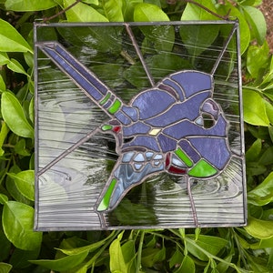 May include: A stained glass window depicting a purple and green robot in a black frame. The robot is in a flying pose with its arms outstretched.