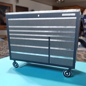 May include: A black metal toolbox with silver accents and wheels. The toolbox has multiple drawers and a side door.