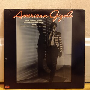 May include: A black and white album cover for the soundtrack to the movie "American Gigolo". The cover features a man in a striped suit standing in a doorway. The text on the cover reads "American Gigolo", "Original Soundtrack Recording", "Music Composed by Giorgio Moroder", "featuring", "Blondie "Call Me" Cheryl Barnes "Love & Passion"