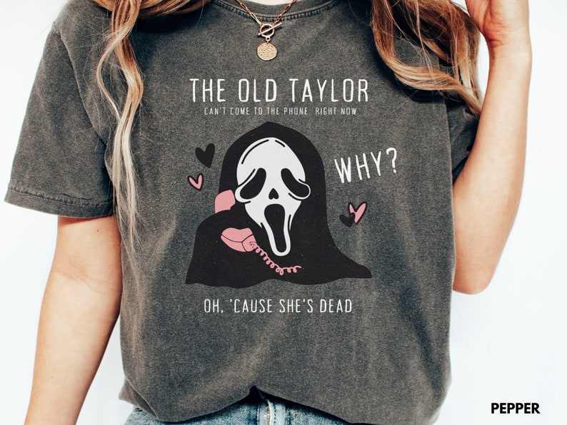 May include: Dark gray t-shirt with a graphic featuring a ghost-like figure holding a pink phone, with text that reads "THE OLD TAYLOR CAN'T COME TO THE PHONE RIGHT NOW WHY? OH, 'CAUSE SHE'S DEAD." Two pink hearts are also included.