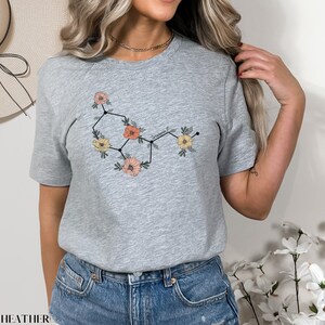 May include: A gray t-shirt with a floral design that resembles a chemical structure. The flowers are pink, yellow, and orange.