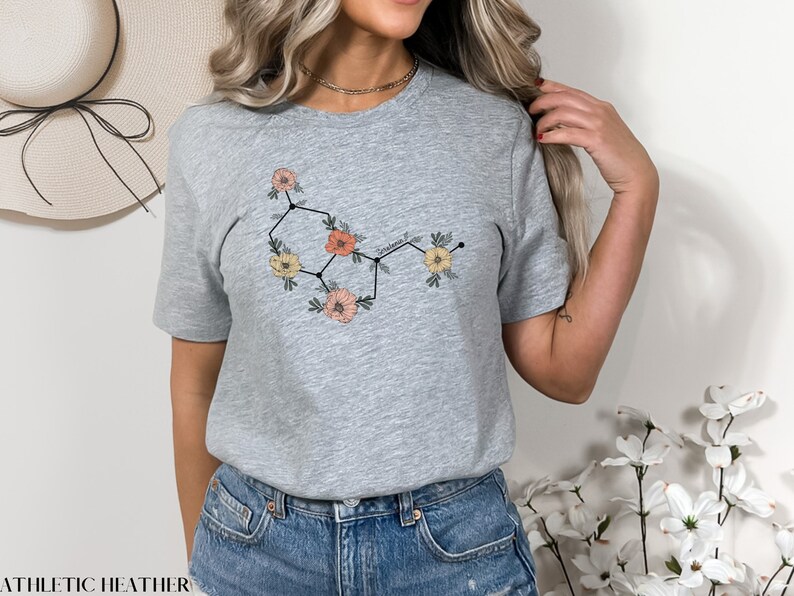 May include: A gray t-shirt with a floral design that resembles a chemical structure. The flowers are pink, yellow, and orange.