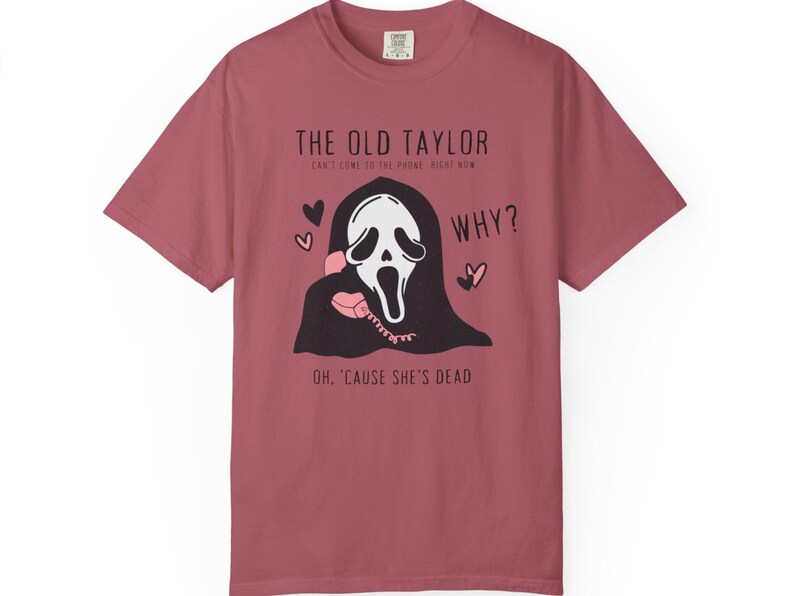 May include: Dusty rose t-shirt featuring a graphic of a ghost-like figure holding a pink telephone. Text includes "THE OLD TAYLOR" and "WHY?" with the phrase "OH, 'CAUSE SHE'S DEAD".