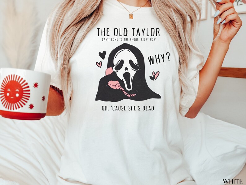 May include: White t-shirt with the text "THE OLD TAYLOR CAN'T COME TO THE PHONE RIGHT NOW WHY? OH, 'CAUSE SHE'S DEAD" and a graphic of a ghost holding a pink telephone. The shirt also features pink hearts.