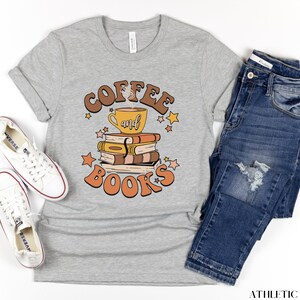 May include: A gray t-shirt with the text "Coffee and Books" in a retro font. The text is surrounded by stars and a cartoon image of a coffee cup on top of a stack of books.