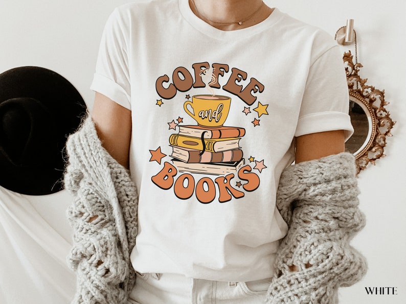 May include: White t-shirt with a retro-style graphic design featuring a coffee cup and books stacked on top of each other. The text reads "Coffee and Books" in a stylized font.