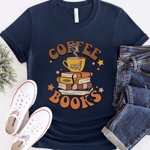 May include: A navy blue t-shirt with the text "Coffee and Books" in brown and orange lettering. The design features a cup of coffee and a stack of books with stars.