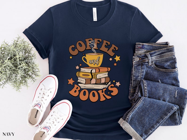 May include: A navy blue t-shirt with the text "Coffee and Books" in brown and orange lettering. The design features a cup of coffee and a stack of books with stars.