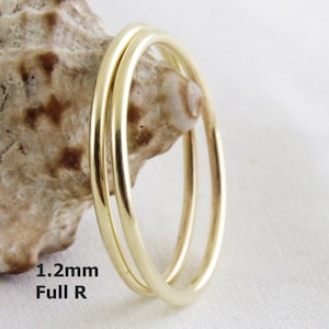 May include: Three gold rings stacked on top of each other. The rings are 1.2mm wide and are made of full round wire. The rings are on a white background.