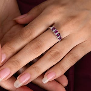May include: A silver band ring with a row of small, rectangular ruby stones and smaller, round white diamonds.