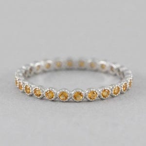 Può includere: Un anello a fascia in argento con una fila continua di piccole pietre preziose citrine gialle rotonde, incastonate in castoni metallici individuali. L'anello ha una forma circolare costante con una finitura metallica lucida e pietre sfaccettate.