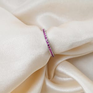 Puede incluir: Un delicado anillo de banda de plata con una fila de pequeñas piedras preciosas rosas.