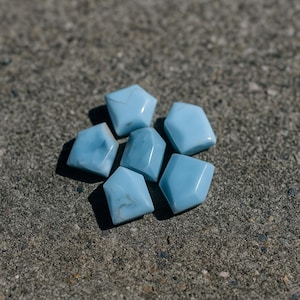 Peut inclure: Un ensemble de sept pierres précieuses bleu clair aux formes irrégulières et facettées. Les pierres sont disposées sur une surface grise et texturée. Les pierres ont un aspect poli et projettent des ombres.