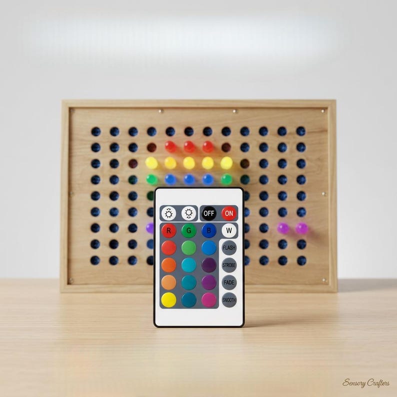 May include: A rectangular light board with a light-colored wooden frame featuring a grid of circular holes. Some holes contain illuminated pegs in red, yellow, blue, green, and purple. A white remote control with twenty-four buttons is in front.