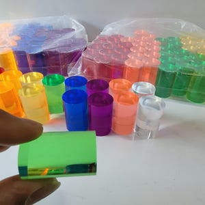 Op de afbeelding: Assortiment van kleurrijke acrylcilinders in verschillende maten. De cilinders zijn gerangschikt in rijen en kolommen, waarbij sommige op elkaar gestapeld zijn. De cilinders zijn gemaakt van helder acryl en hebben een verscheidenheid aan kleuren, waaronder rood, oranje, geel, groen, blauw, paars en helder.