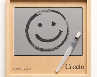May include: A wooden framed art piece featuring a gray drawing board with a black smiley face. A white water brush is placed on the right side of the board. The word "Create" is printed in black on the bottom right corner.