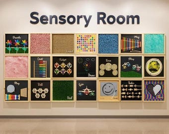 May include: A wall display labeled "Sensory Room" features framed panels with various textures and interactive elements. The panels include colorful pinwheels, abacuses, and drawings, designed for sensory exploration and play. The display is designed for educational or therapeutic purposes.