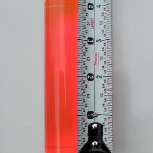Op de afbeelding: Een feloranje acrylstaaf gemeten met een meetlint. De staaf is 7 cm lang.
