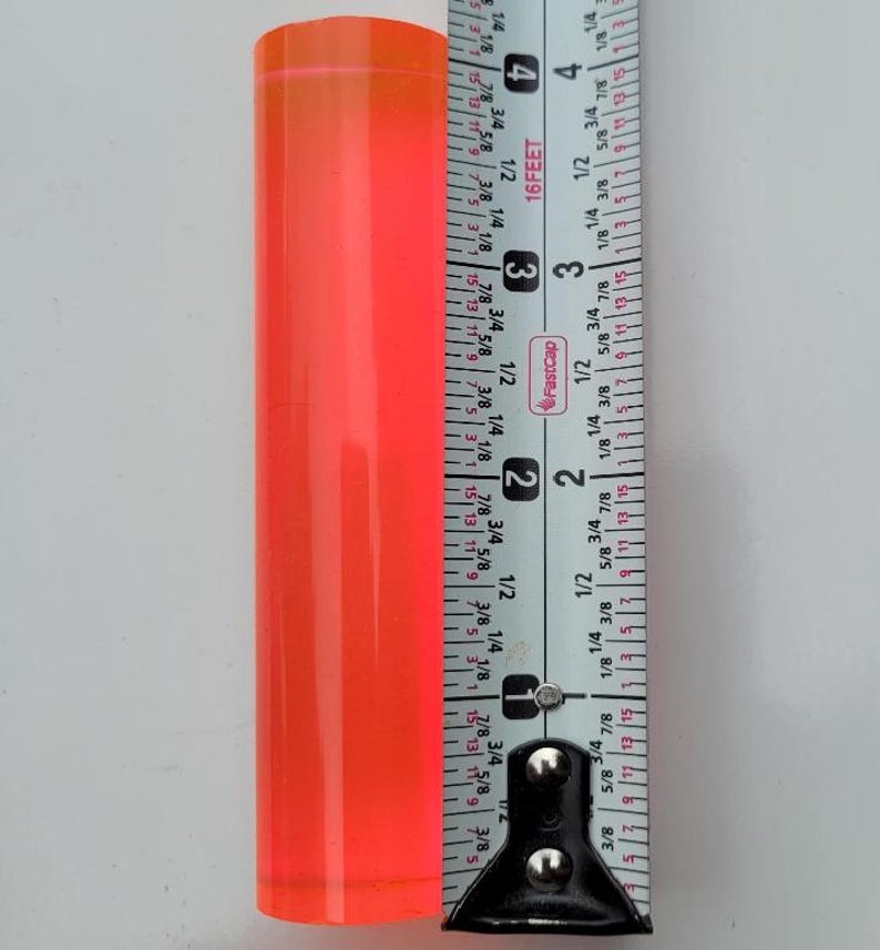 Op de afbeelding: Een feloranje acrylstaaf gemeten met een meetlint. De staaf is 7 cm lang.