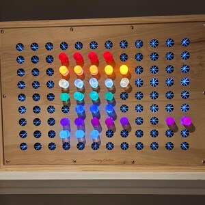 May include: A rectangular light-colored wooden sensory board featuring a grid of circular holes. Many holes contain glowing blue star-shaped lights, while a central section displays a vertical arrangement of colorful pegs in red, orange, yellow, white, green, blue, and purple.