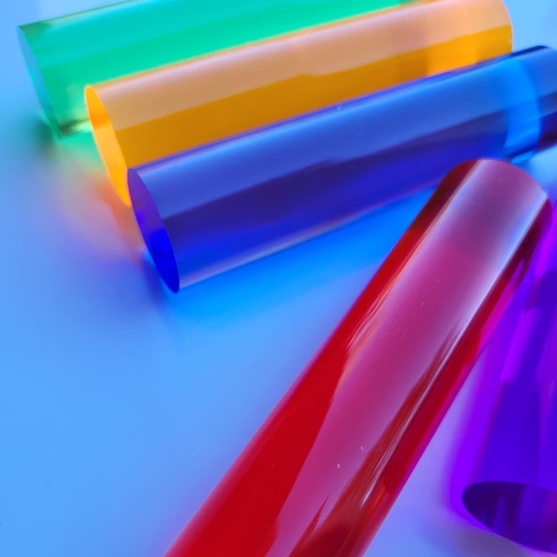 Op de afbeelding: Vijf transparante acryl staven in verschillende kleuren: groen, oranje, blauw, rood en paars. De staven zijn in een waaier vorm gerangschikt, met de groene staaf bovenaan en de paarse staaf onderaan.