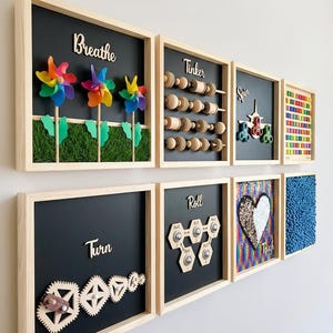 May include: A set of seven square wooden sensory wall panels with black backgrounds. Features include rainbow pinwheels, wooden beads, fidget spinners, a colourful grid, interlocking gears, rolling balls, a sequin heart, and blue textured material.