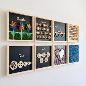 May include: A set of eight square wooden frames mounted on a wall, each featuring sensory activities. Panels include pinwheels, wooden beads, fidget spinners, colourful tiles, interlocking gears, rolling hexagonal pieces, a sequin heart, and blue texture.