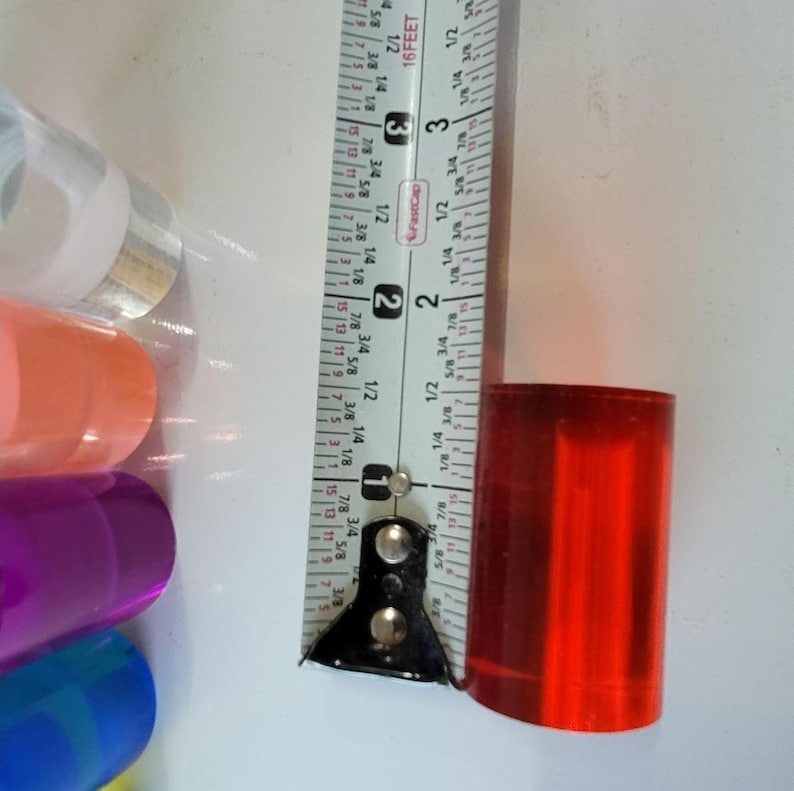Op de afbeelding: Een rode acrylstaaf gemeten met een liniaal. De liniaal toont metingen in inches en voet. De staaf is ongeveer 1 inch in diameter.