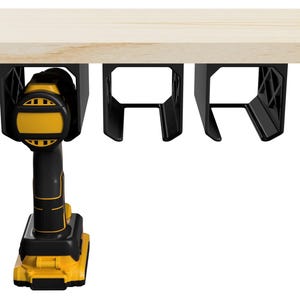 Puede incluir: Un taladro inalámbrico negro y amarillo está montado en un soporte negro debajo de una superficie de madera. Se ven dos soportes negros adicionales, diseñados para guardar herramientas. El taladro es amarillo y negro.