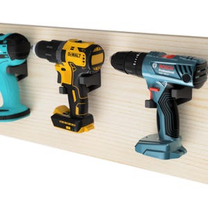May include: Three cordless drills mounted on a wooden wall. The drills are yellow and black, blue and black, and teal and black. The drills are labelled "DEWALT" and "BOSCH Professional".