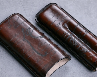 May include: Two brown leather cigar cases with a decorative pattern of script and leaves. The cases are open and empty.