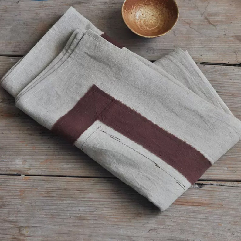 May include: A folded linen kitchen towel with a wide brown stripe down the centre. The towel is folded in half and has a rustic, natural look.