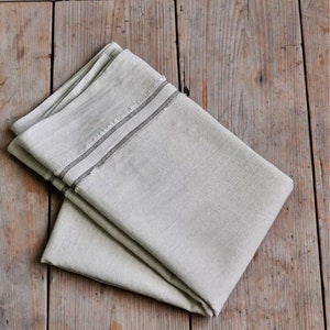 May include: A folded linen tea towel with a black trim. The towel is folded in half and has a subtle texture.