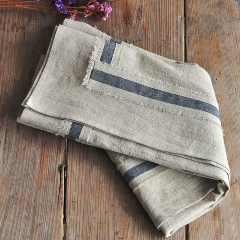 May include: A folded linen tablecloth with a frayed edge and two dark blue stripes running along the length of the fabric.